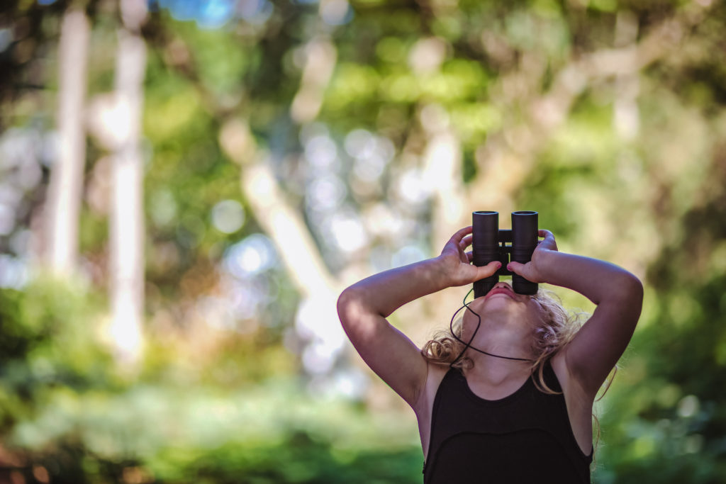 girl viewing nature with binoculars during camping trip